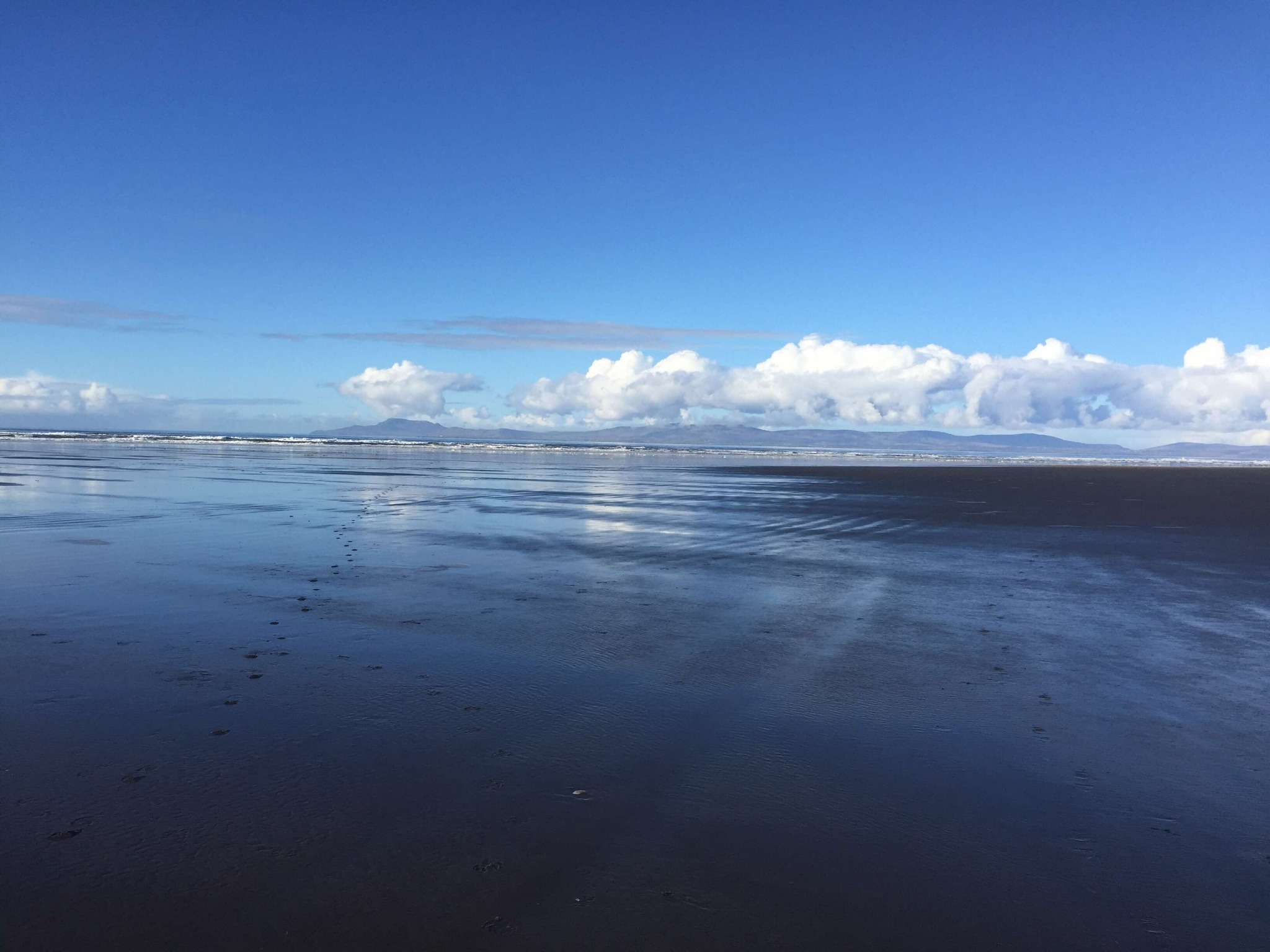 Reflective beach with mountains and clouds